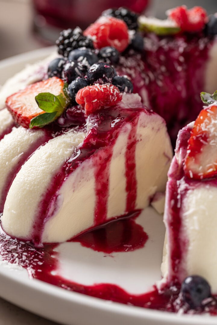 Close-up of Brazilian coconut flan topped with berry sauce, fresh berries, and shredded coconut.