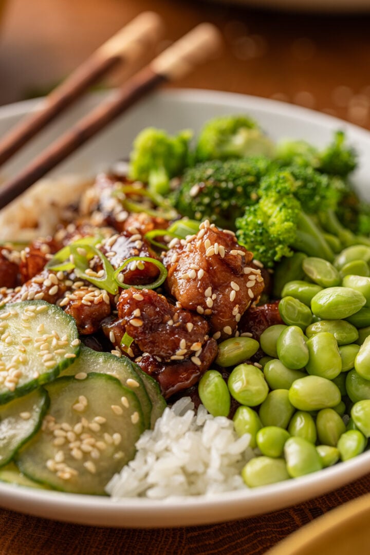 Close-up of glossy homemade teriyaki chicken served over rice with sesame seeds and green onions.