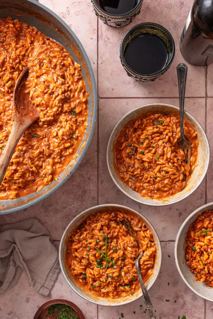 Overhead view of creamy ground beef orzo served in bowls with skillet in the background.