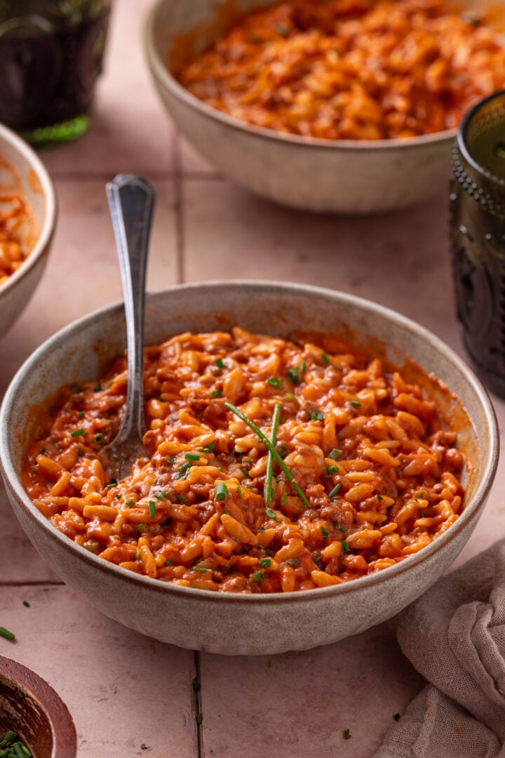 Bowl of creamy ground beef orzo topped with chives and a spoon standing upright.