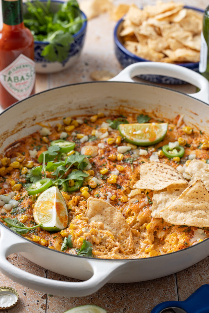 Skillet of Mexican street corn dip served with tortilla chips, lime wedges, and fresh cilantro