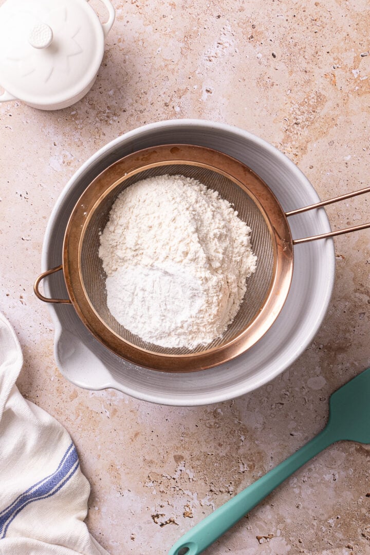 Flour and baking powder sifted into a bowl for churro cake batter.