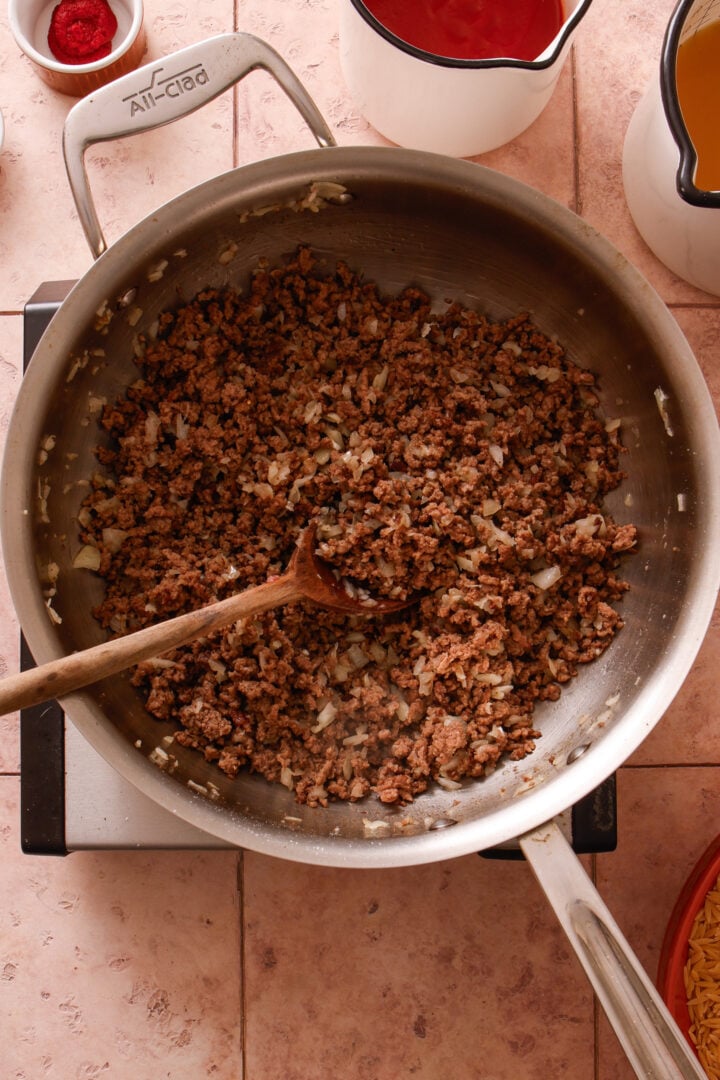 Ground beef and onions cooking together in a skillet for creamy beef orzo.