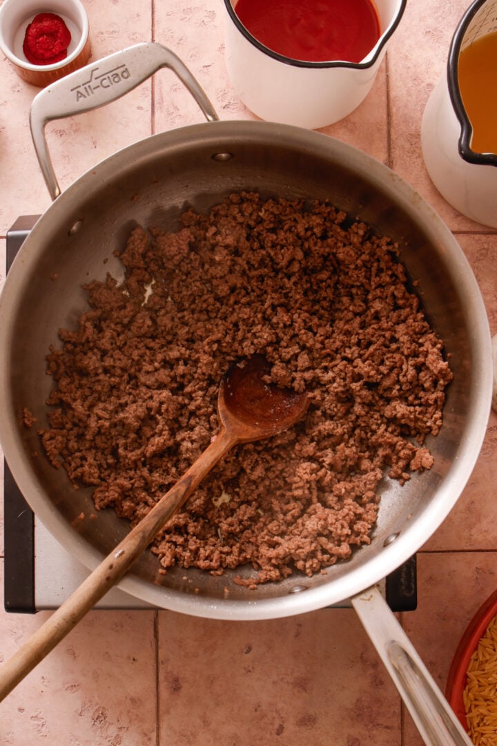 Ground beef browning in a large skillet for creamy ground beef orzo.