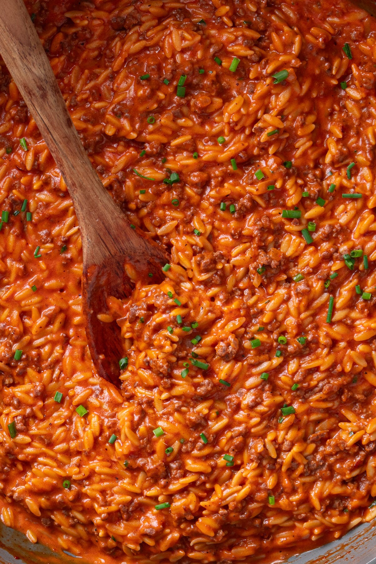 Close-up of creamy ground beef orzo garnished with chives in a skillet.