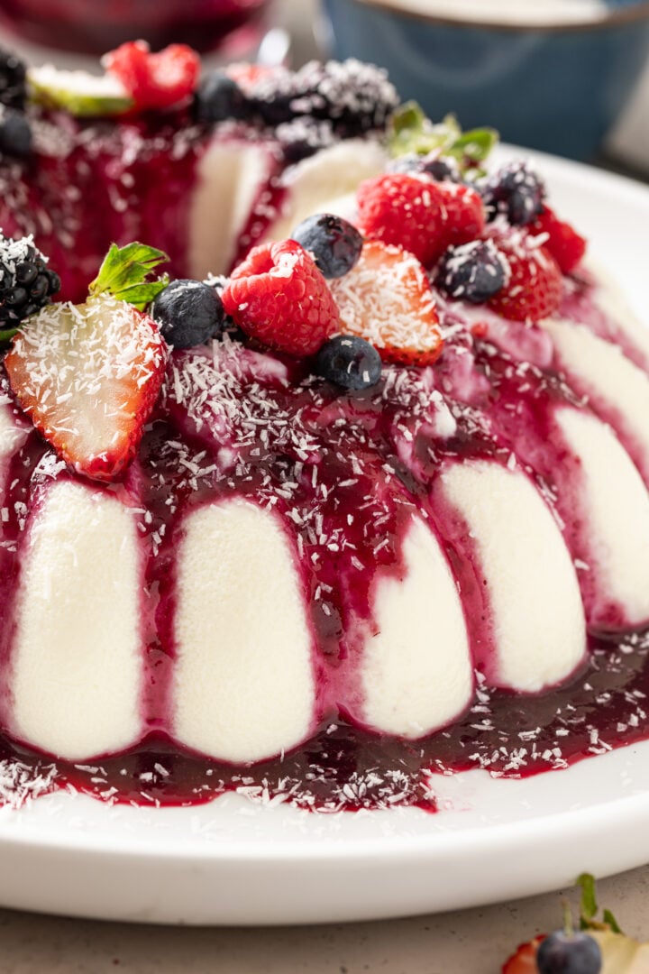 Close-up of coconut flan with berry sauce, fresh berries, and shredded coconut.