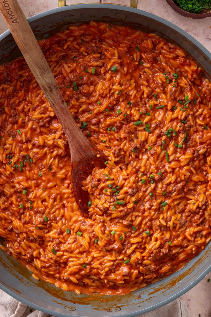 Close-up of creamy tomato ground beef orzo in a skillet with fresh chives.