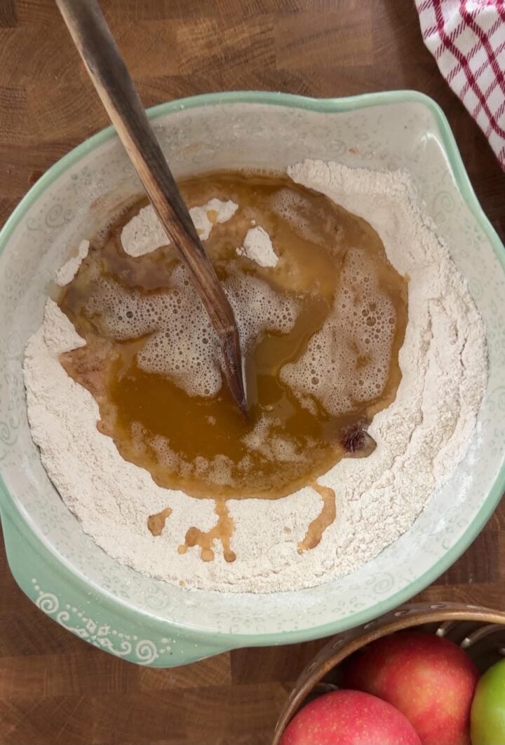 Browned butter being added to the dry ingredients for apple crumble bars in a large mixing bowl.