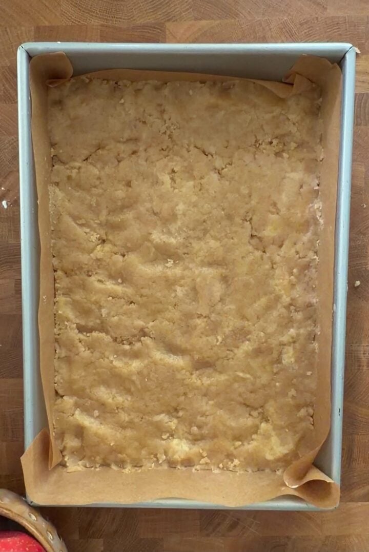 Brown butter crust pressed into a parchment-lined metal baking pan before par-baking.