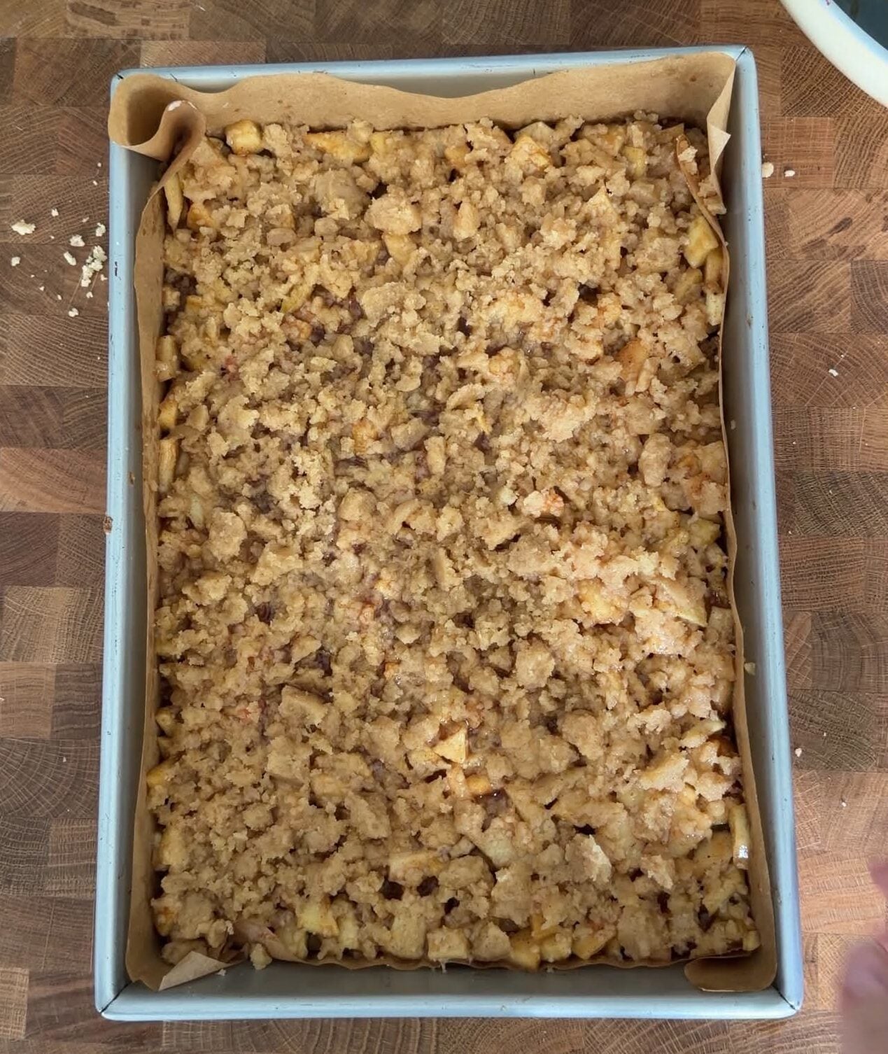 Apple crumble bars assembled with cinnamon apple filling and brown butter crumble topping before baking.