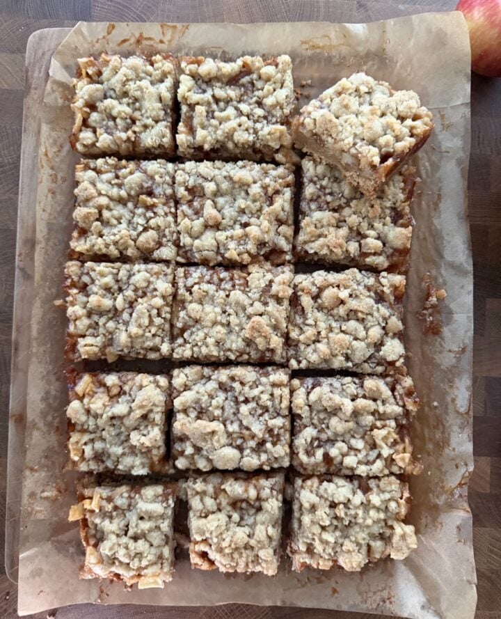 Freshly baked apple crumble bars cut into squares on parchment paper.