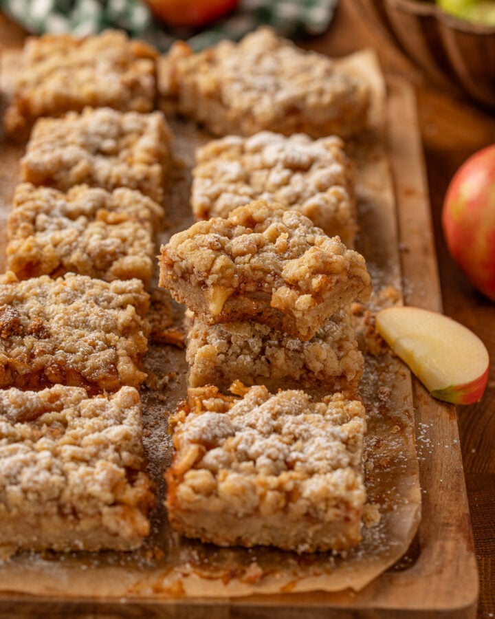 Apple crumble bars with cinnamon apple filling, brown butter crust and powdered sugar on a wooden board.