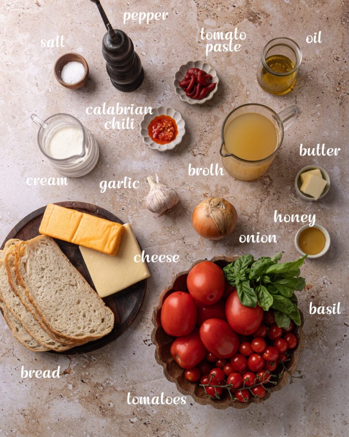 Ingredients for roasted tomato soup and grilled cheese croutons, including tomatoes, basil, garlic, onion, broth, cream, chilies, bread, cheddar, and Gruyère.